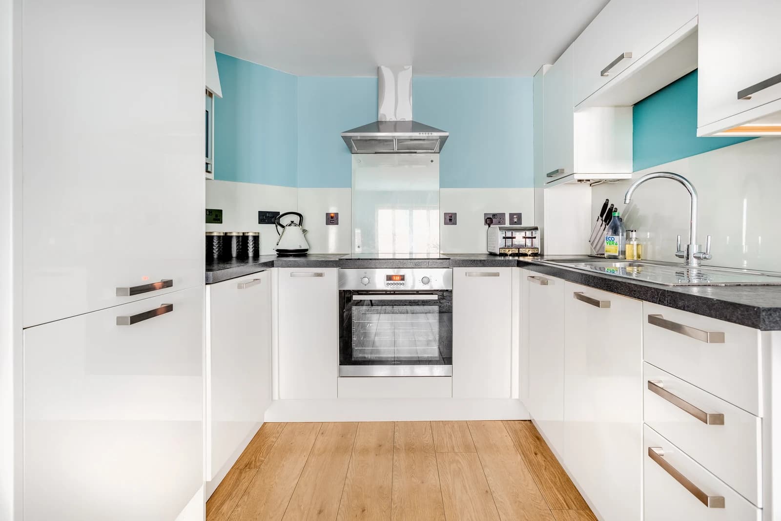 White L-shaped kitchen with integrated appliances and blue walls at Station Road Flat 52a