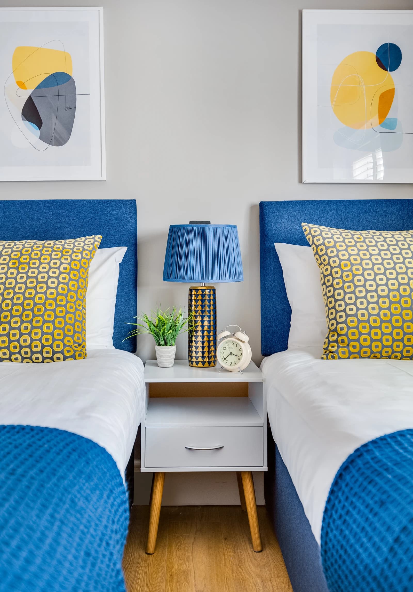 Bedroom with blue headboard, yellow patterned cushions and lamp at Station Road Flat 52a
