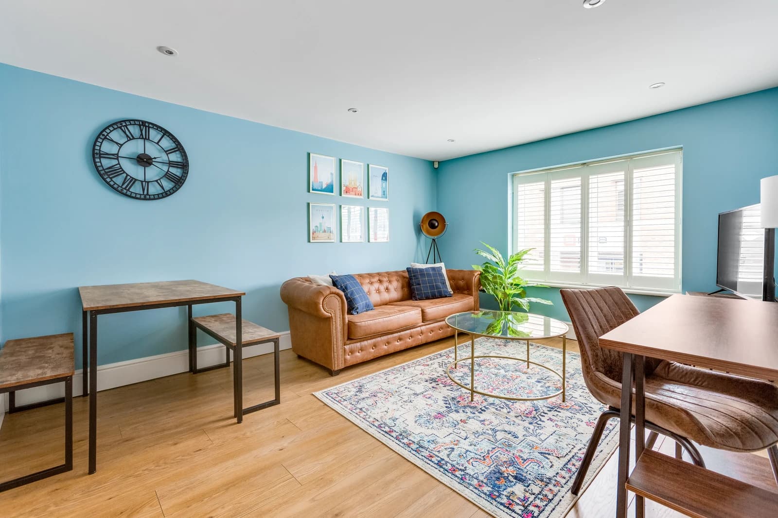 Open-plan living area with tan sofa, dining table and blue wall at Station Road Flat 52a