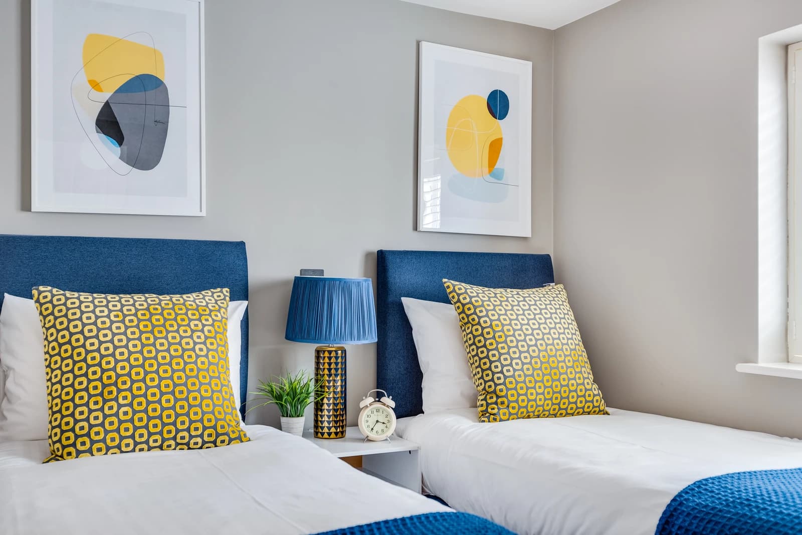 Two single beds with blue and yellow cushions and bedside lamps at Station Road Flat 52a, Egham