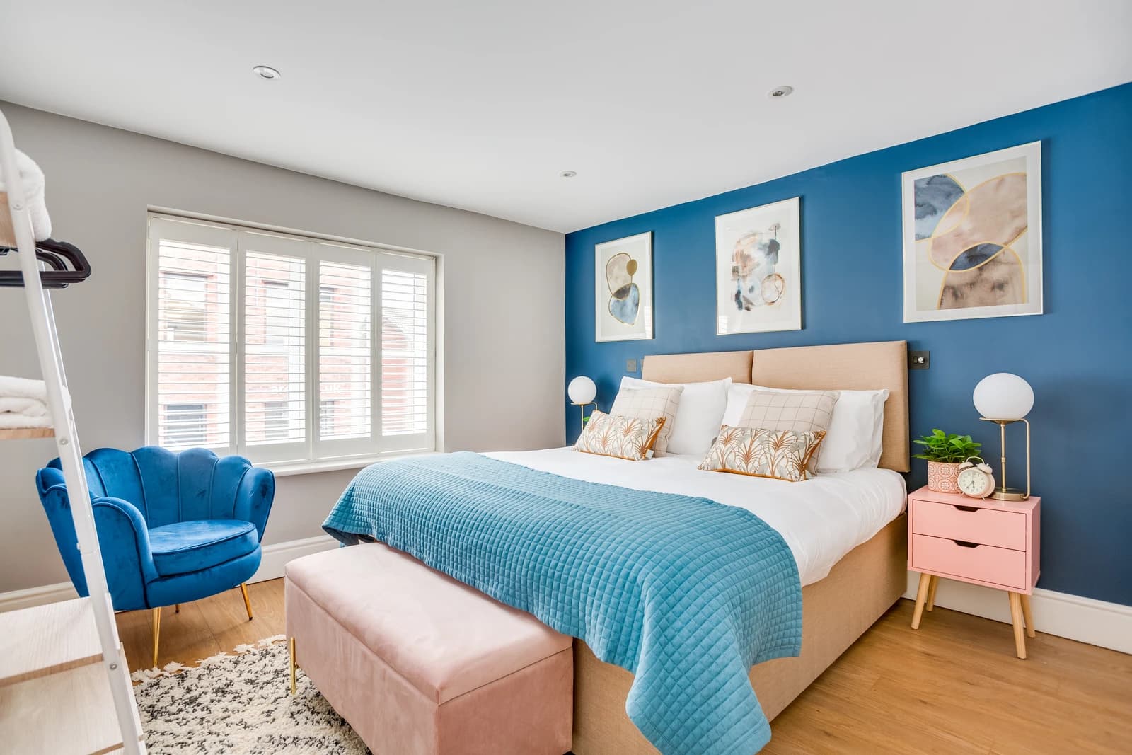 King-size bed with pink bedding and blue accent chair in the second bedroom at Station Road Flat 52a