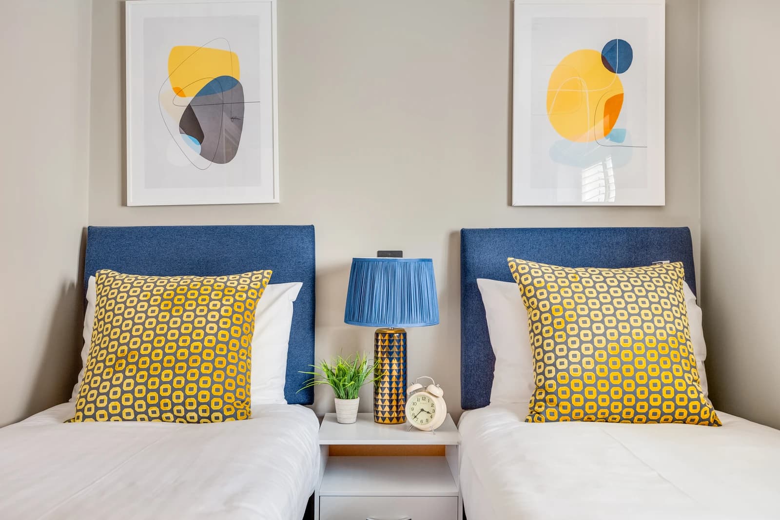 Two single beds with blue cushions, books and bedside plant at Station Road apartment, Egham