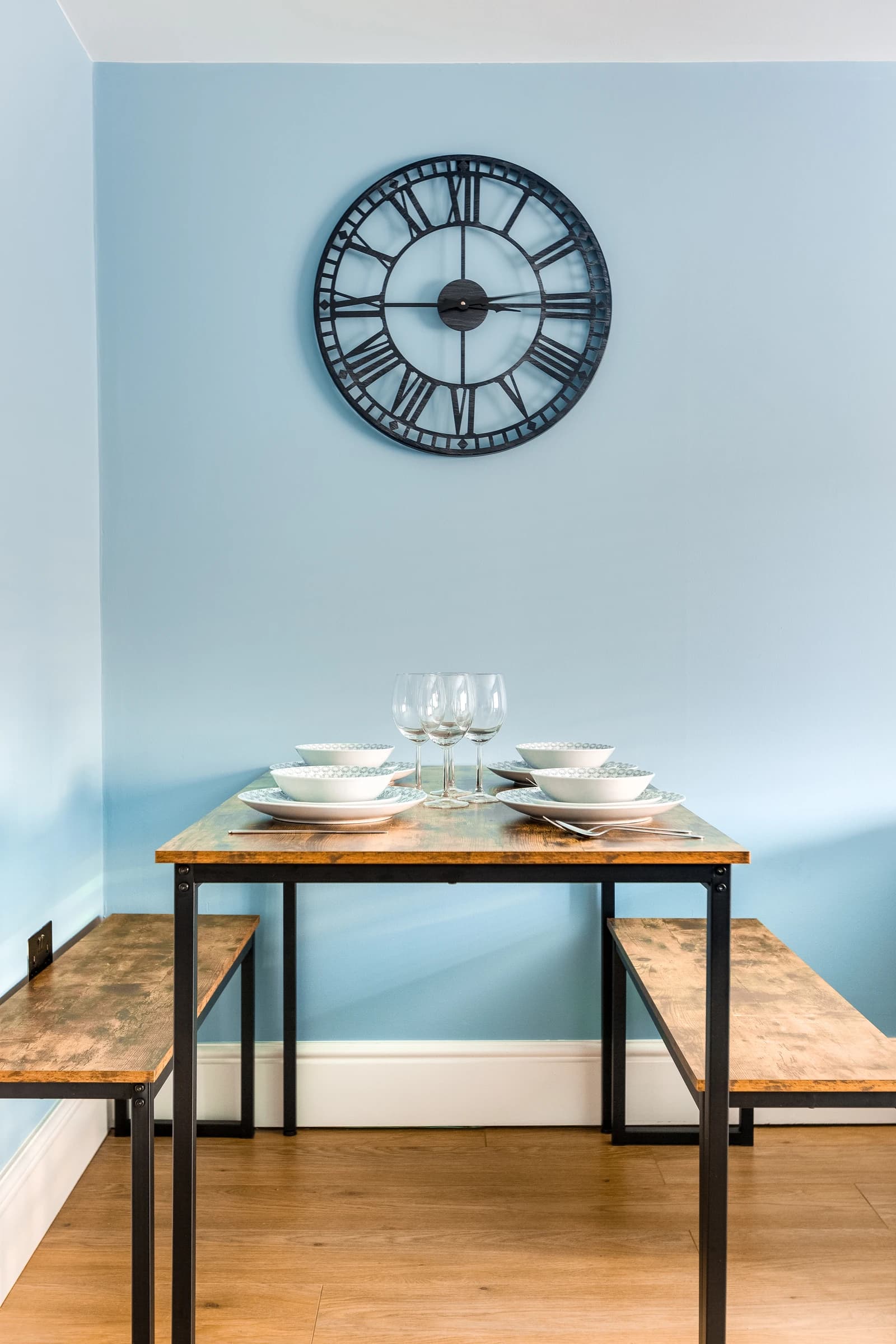 Dining table set for four with wine glasses and blue feature wall at Station Road, Egham