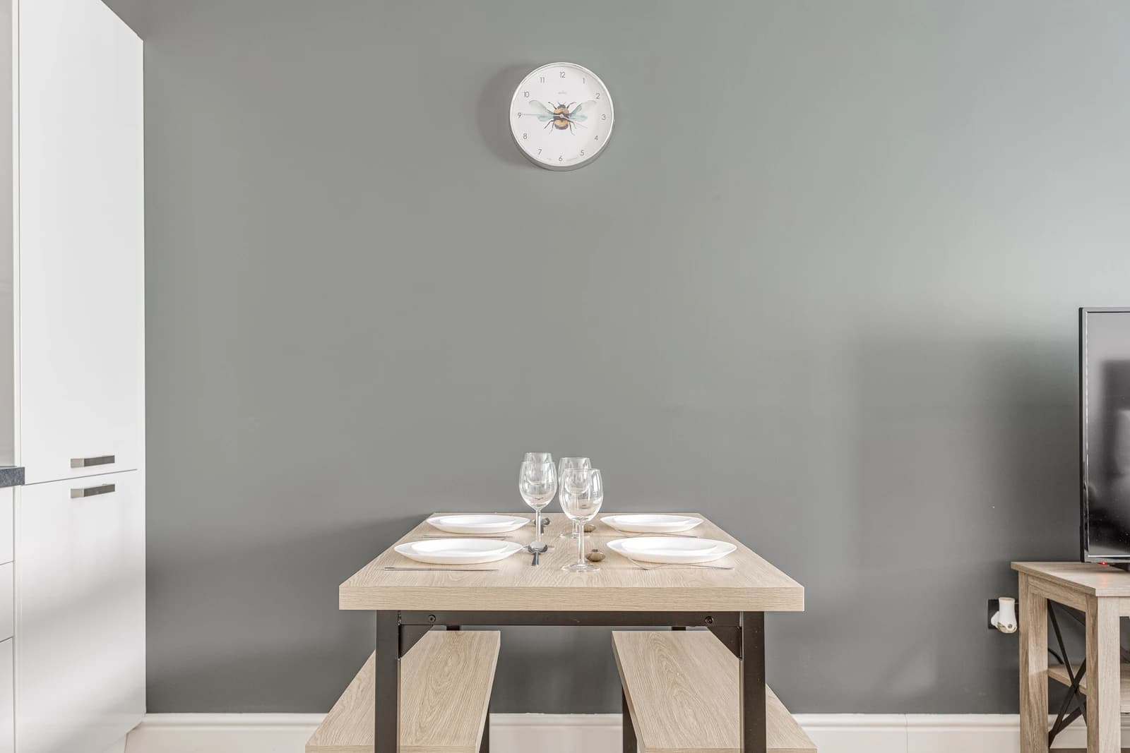 Dining area with grey feature wall, wooden table and wine glasses at Boon House apartment