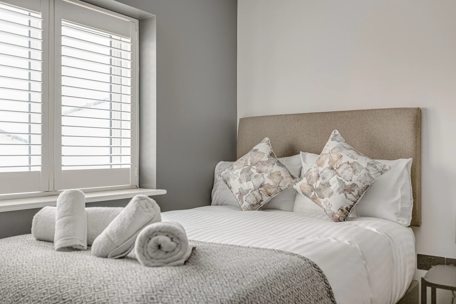 Double bed with neutral bedding, cushions and rolled towels at Boon House serviced apartment