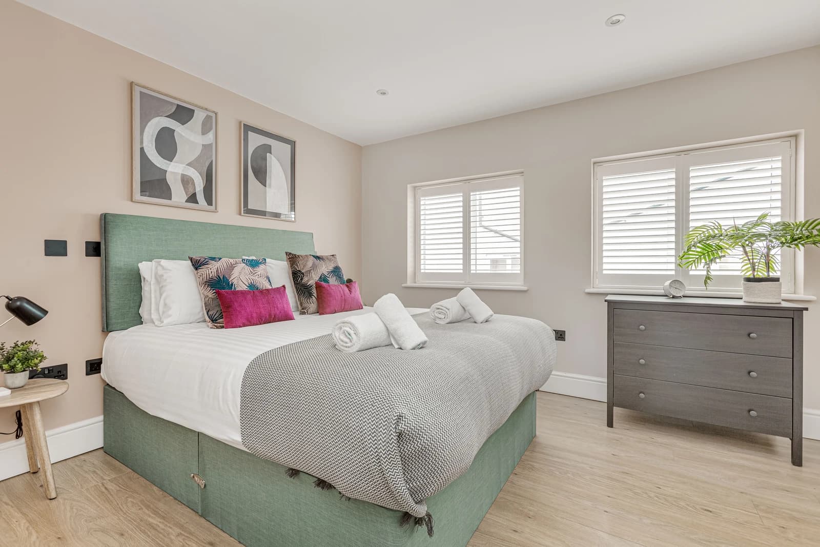 Colourful bedroom with teal headboard, pink cushions and modern artwork at Boon House, Egham
