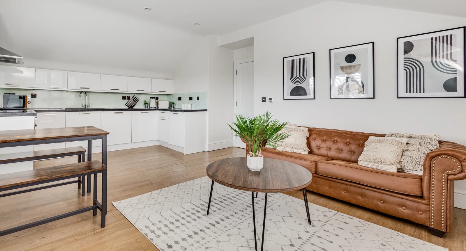 Living area with tan leather sofa, plants and modern artwork at Boon House serviced apartment