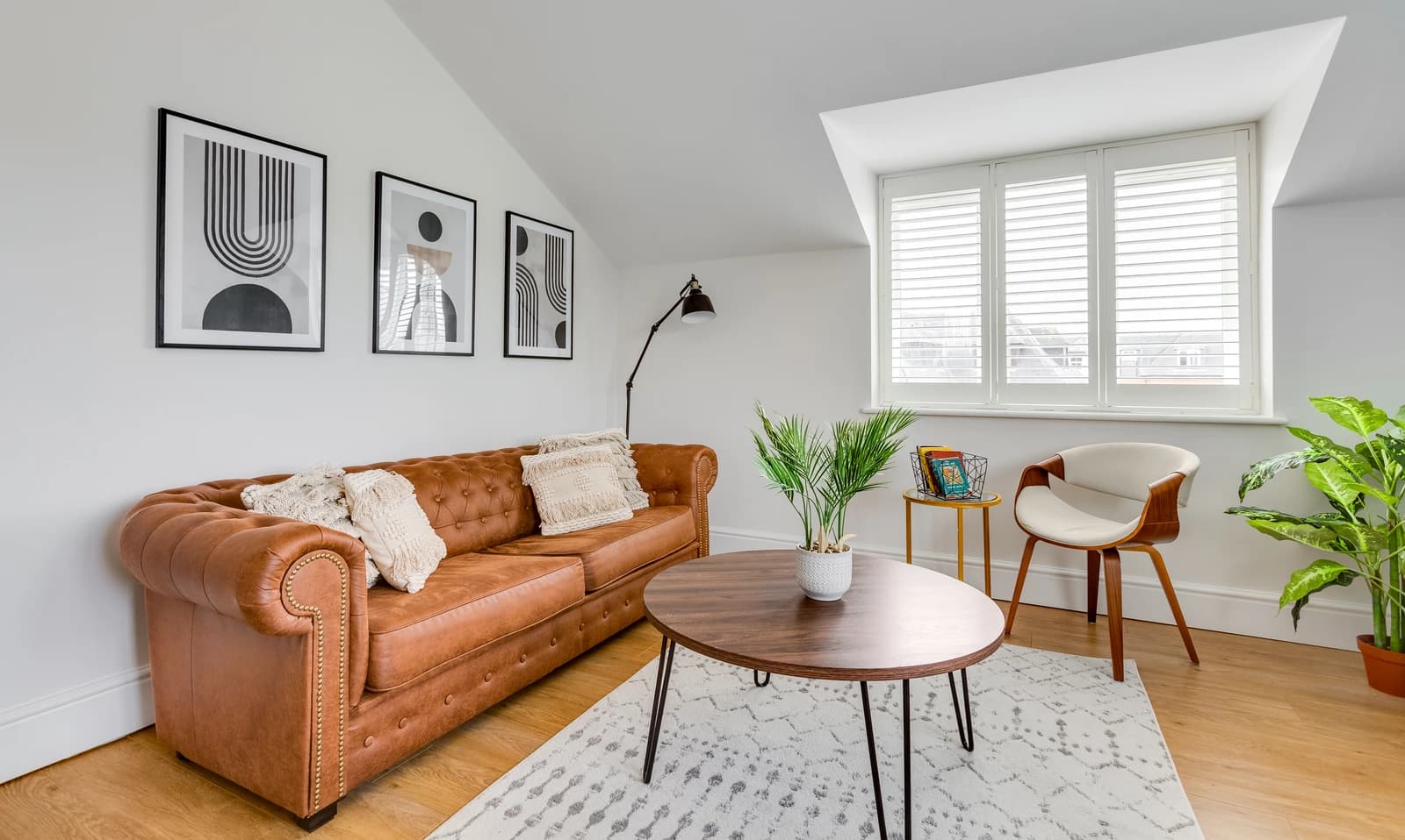 Living room with tan leather sofa, round coffee table and indoor plants at Boon House, Egham