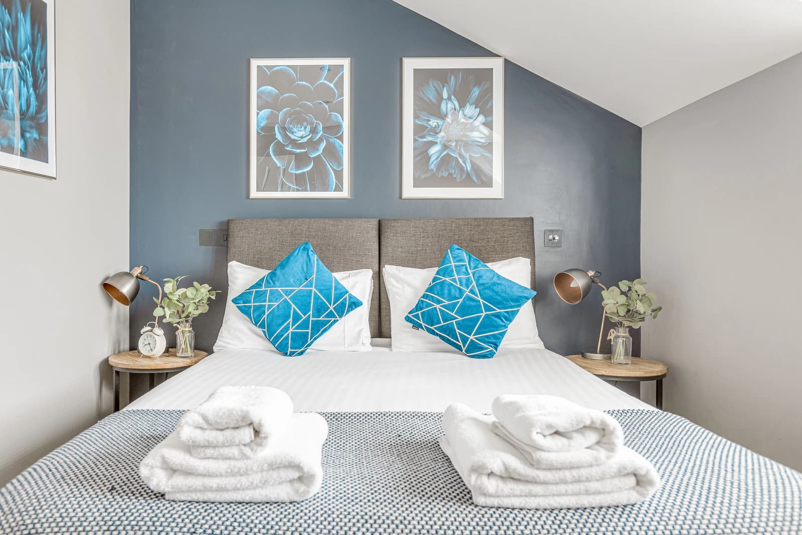 King-size bed with blue cushions, towels and framed artwork at Boon House Flat 4 apartment