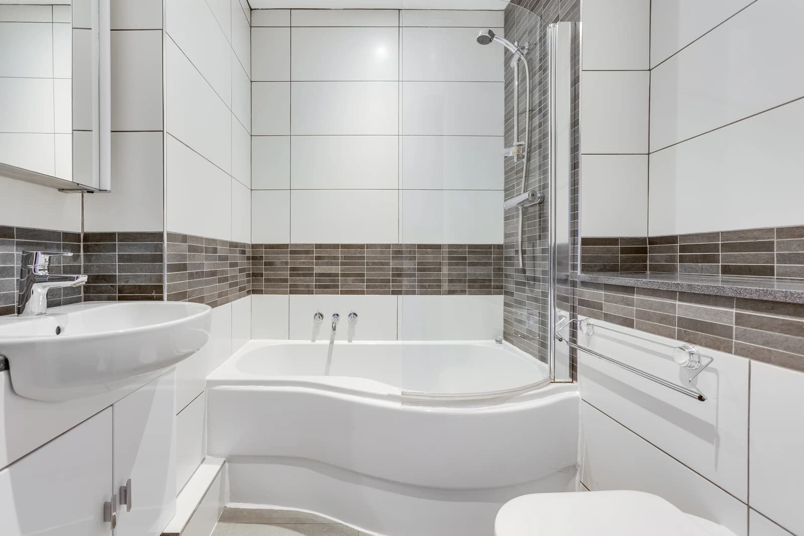 Modern bathroom with corner bath, shower screen and grey tiles at Boon House Flat 4, Egham