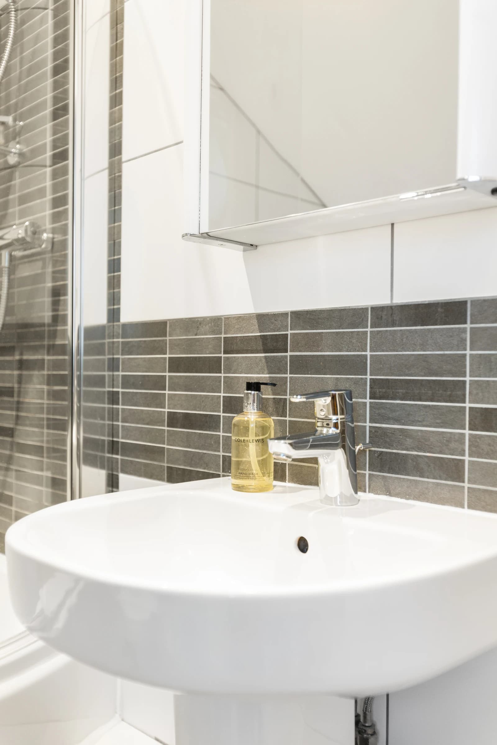 Bathroom shelf with soap dispensers and grey wall tiles at Boon House Flat 3, Egham