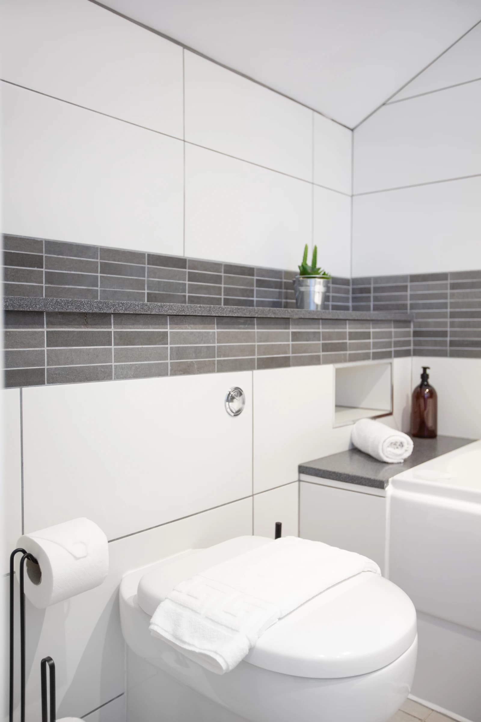 Grey tiled bathroom with towel rail and bath at Boon House serviced apartment, Egham