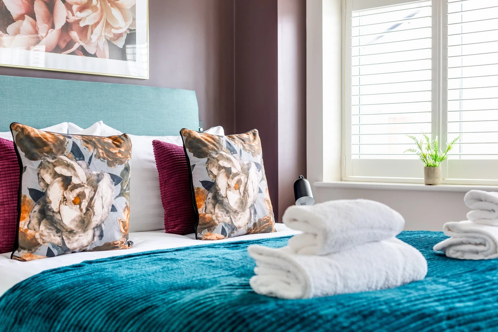 Close-up of bed with teal throw, towels and decorative cushions at Boon House, Egham